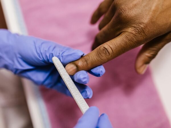 Acessórios de manicure e biossegurança Profissional usa luvas nitrílicas e lixa descartável em cliente, reforçando a segurança do atendimento 