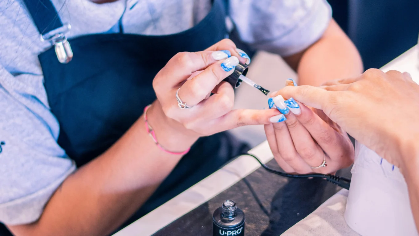 Manicure-aplicando-top-coat-Risqué-em-unhas-decoradas-com-design-azul-e-branco